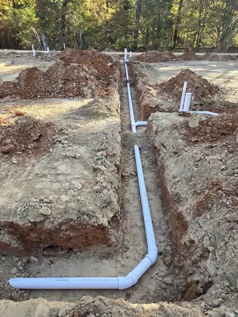 White PVC line laid in a trench of red soil on a new-build lot