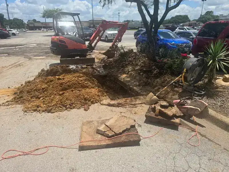 Mini excavator digging out a broken line beside a parking lot