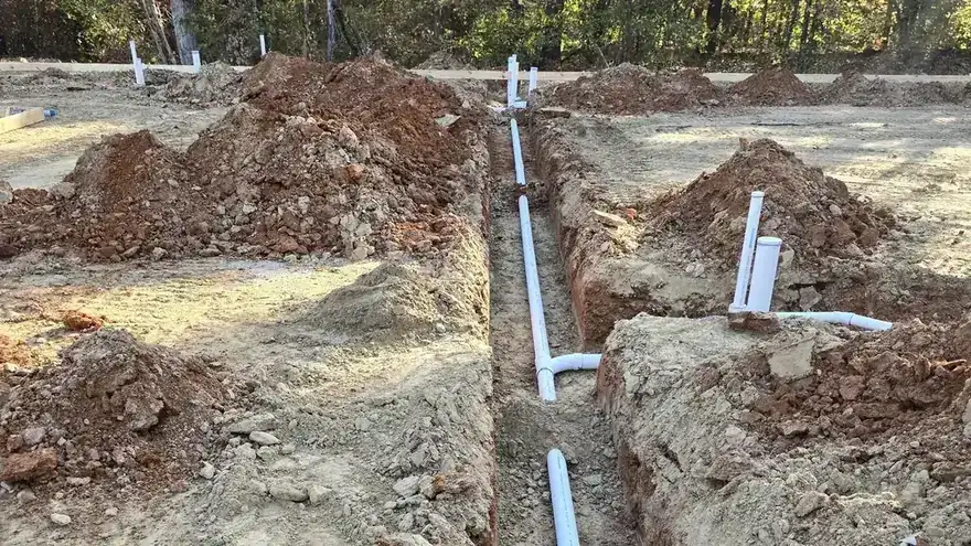 New white drain line running down an open trench toward the treeline