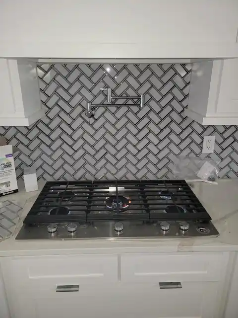 Gas cooktop under a herringbone tile backsplash