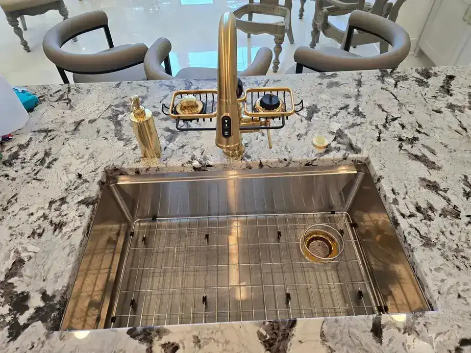 Kitchen workstation sink with a brushed gold faucet on granite