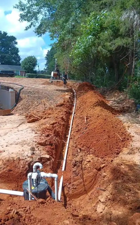Long trench with a new white sewer line and cleanout in red clay